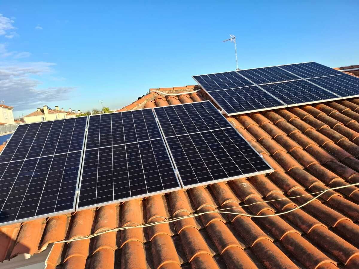 Paneles solares instalados en un techo de tejas rojas contra un cielo azul.