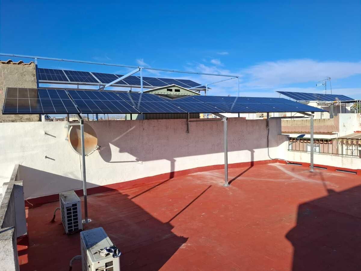 Paneles solares instalados en un tejado, sostenidos por estructuras metálicas, con una superficie roja brillante. Cielo azul.