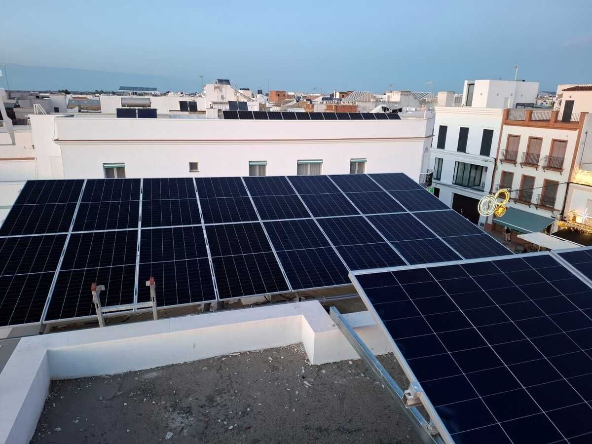 Paneles solares instalados en un tejado blanco de una ciudad, con edificios al fondo.