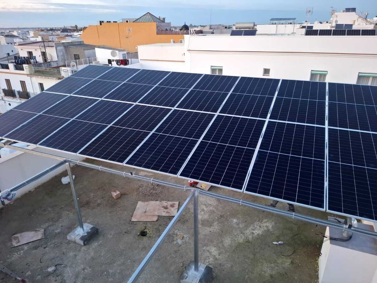 Paneles solares instalados en un tejado, sostenidos por marcos de metal, con edificios al fondo.