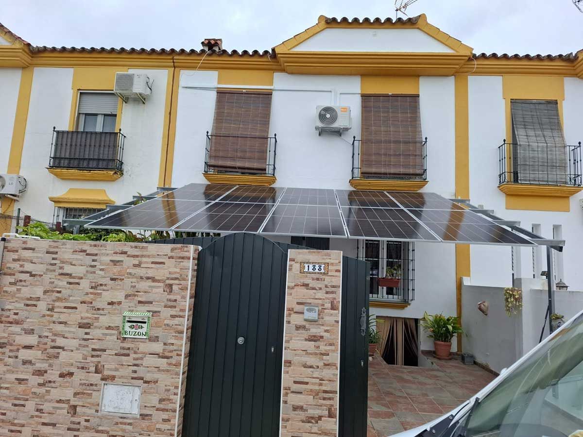 Casas adosadas con paneles solares sobre una verja. Fachada amarilla y blanca, persianas marrones.