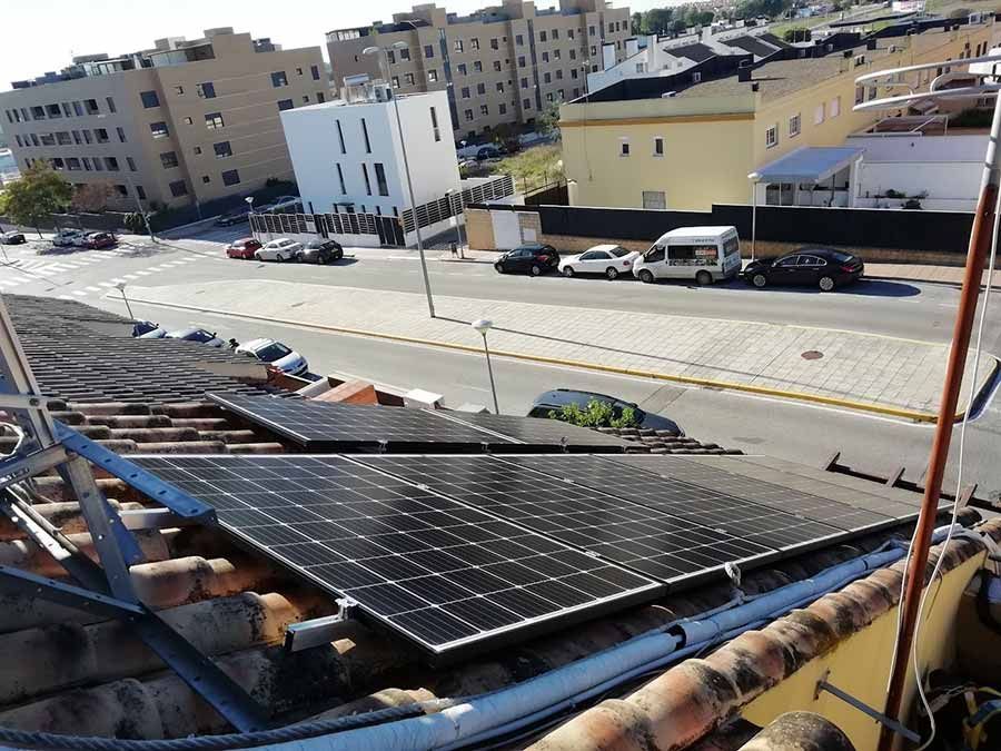 Paneles solares en la azotea de un edificio con vista a una calle con autos estacionados y otros edificios.