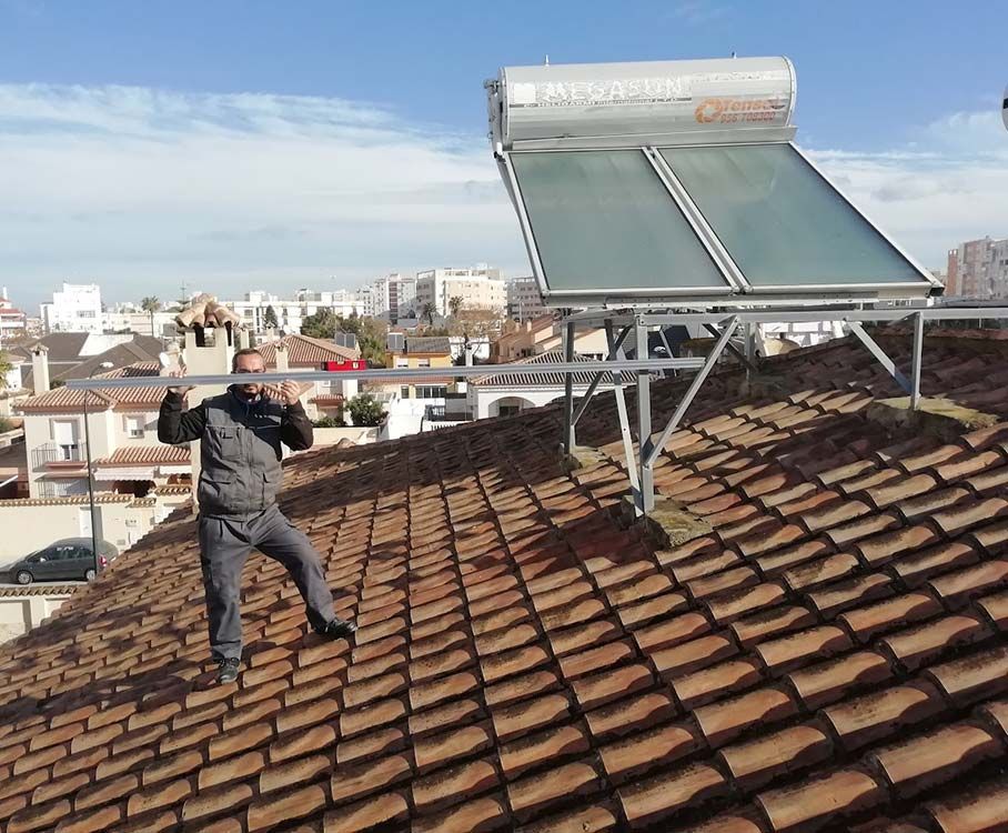 Hombre instalando un calentador solar de agua en la azotea. Vista del horizonte de la ciudad al fondo. Día soleado.