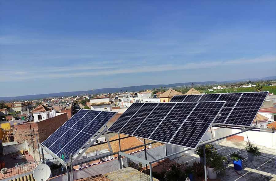 Paneles solares en un tejado, orientados hacia un cielo azul con vistas a una ciudad con edificios y campos verdes.
