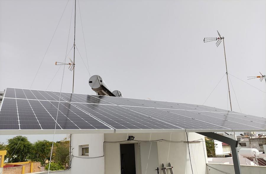 Paneles solares en un tejado con antenas y un calentador de agua, bajo un cielo nublado.