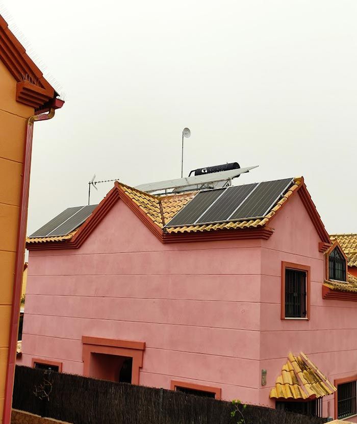 Casa rosa con paneles solares en el techo y una valla oscura en el frente.