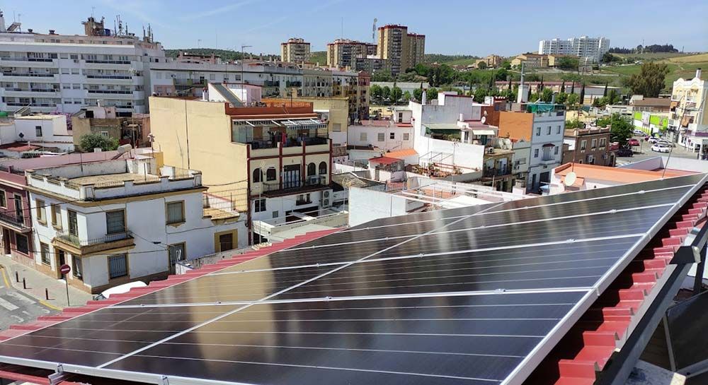Paneles solares sobre un techo rojo con vistas a una ciudad con edificios blancos y tostados bajo un cielo azul.