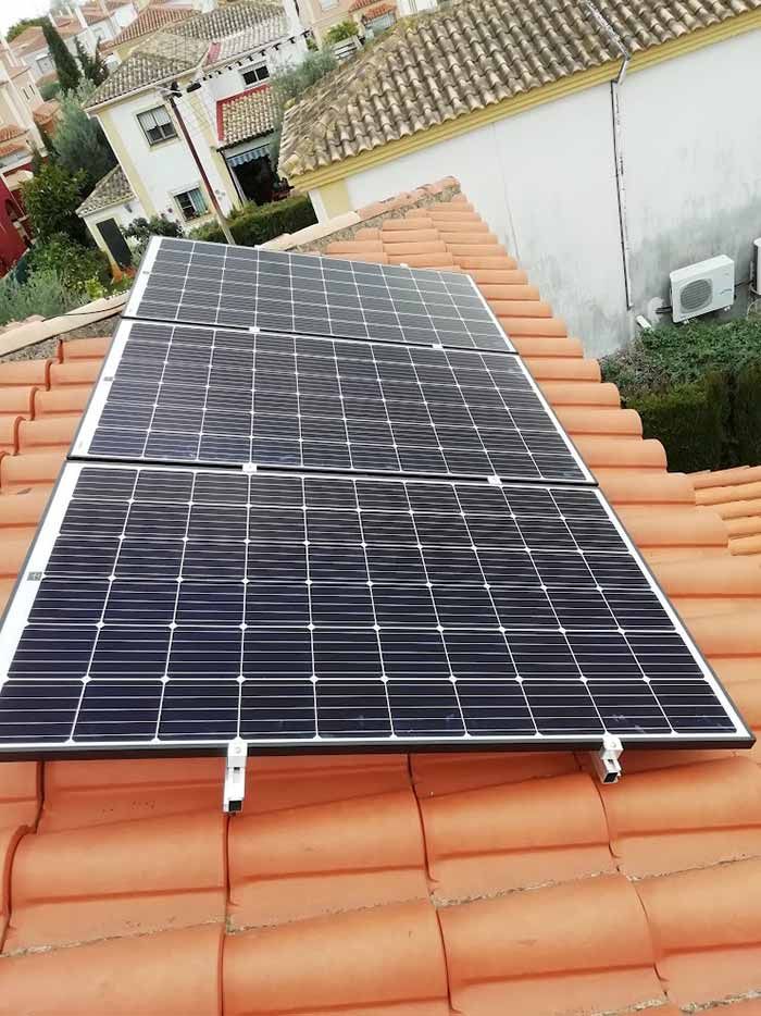 Paneles solares instalados en un techo de tejas rojas en una zona residencial.