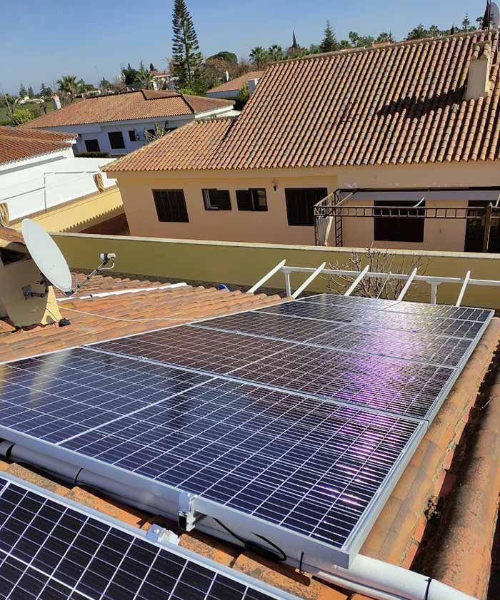 Paneles solares instalados en un techo de tejas de terracota de una casa beige, en un entorno exterior soleado.