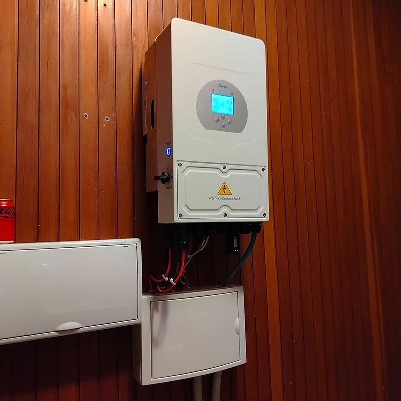 Inversor de energía solar montado en una pared de madera, con cajas eléctricas y cableado asociados.