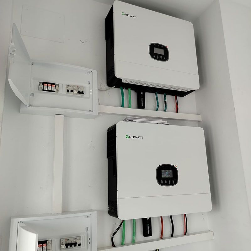 Dos inversores solares blancos montados en una pared con cajas eléctricas y cableado.