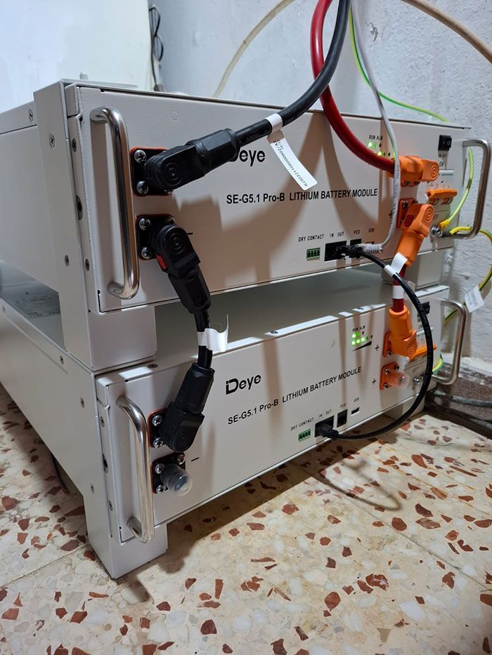 Dos módulos de batería de litio Deye apilados, conectados con cables negros. Conectores naranja y negro visibles.