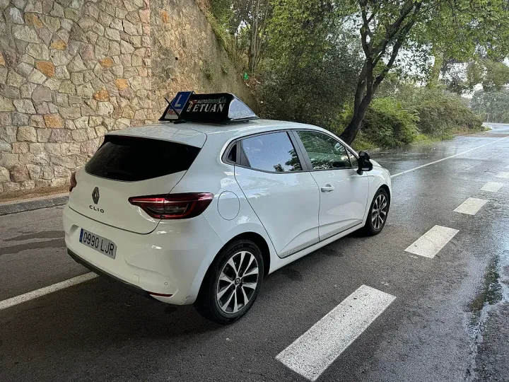 Un coche blanco está aparcado al costado de la carretera junto a un muro de piedra.