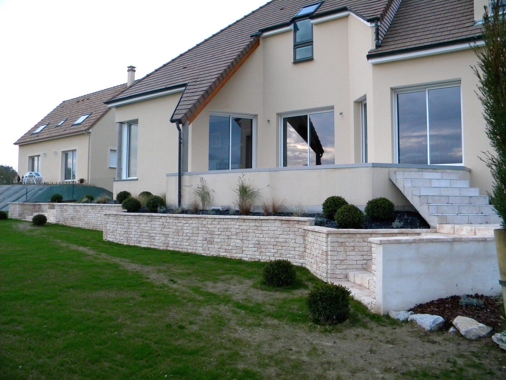 Petit muret de soutènement devant une grande maison
