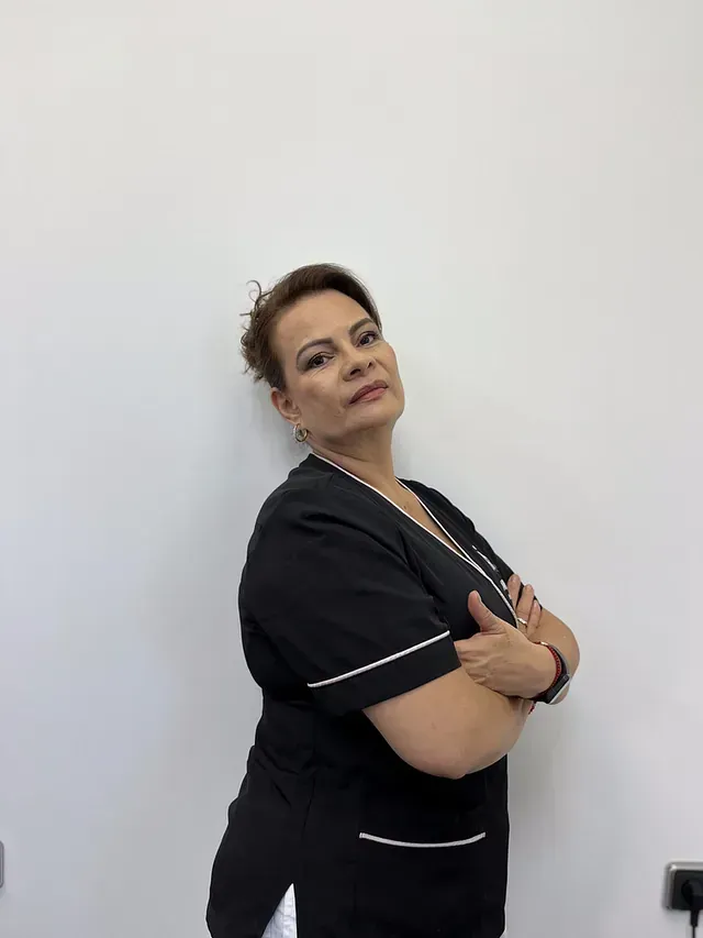 Una mujer con un uniforme negro está parada frente a una pared blanca con los brazos cruzados.