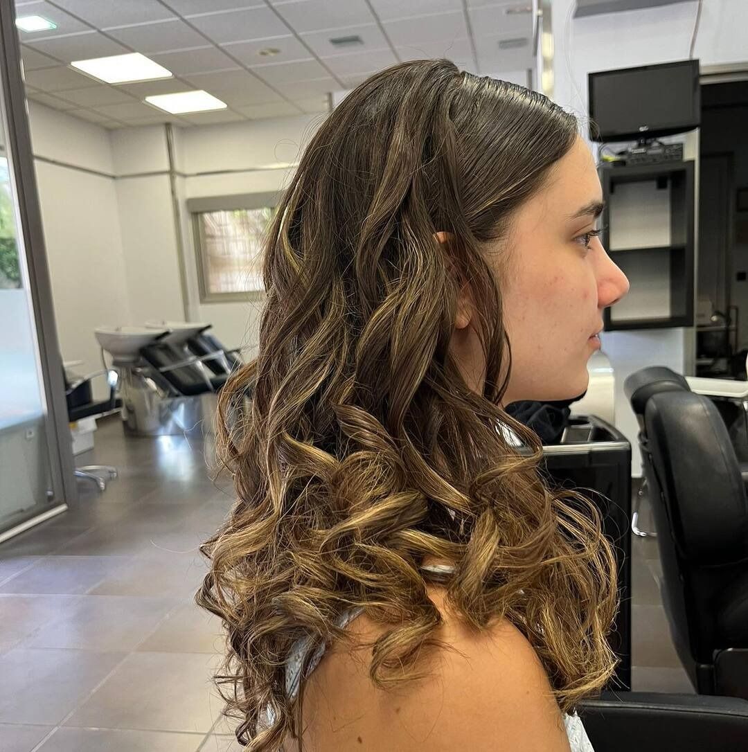 Una mujer con cabello largo y rizado está sentada en una silla en un salón.