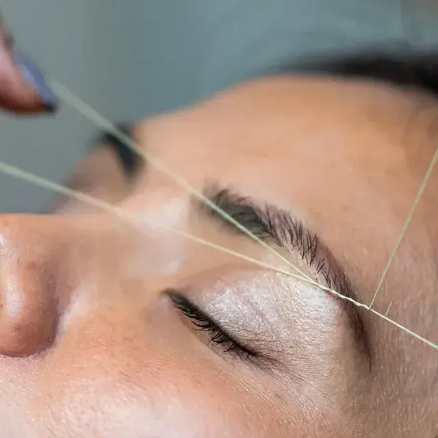 Una mujer se está depilando las cejas con un hilo.