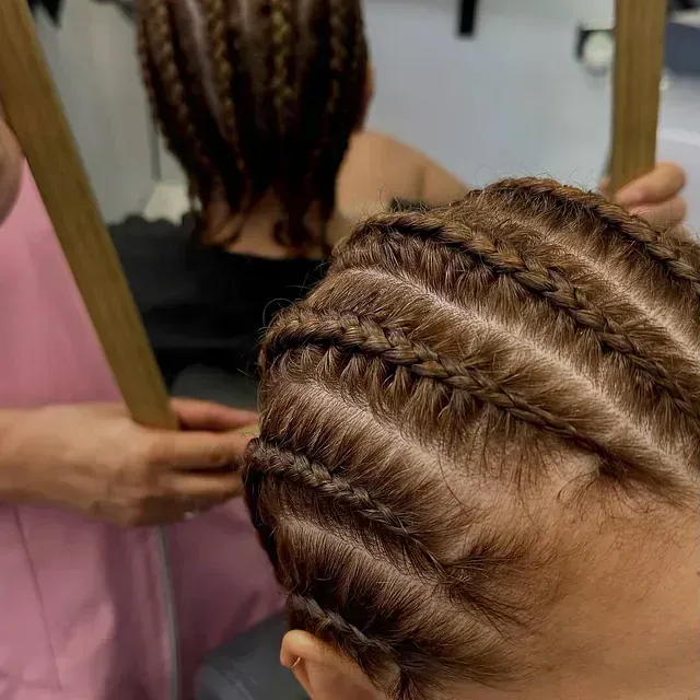 Una mujer se trenza el cabello frente a un espejo.
