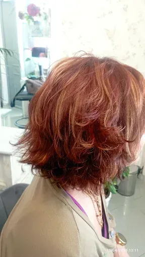 Vista lateral de una persona con cabello castaño rojizo, ondulado y hasta los hombros, sentada en una silla de peluquería.