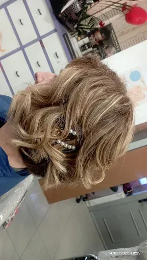Primer plano de un peinado rubio ondulado con una pinza decorativa en un salón de belleza.