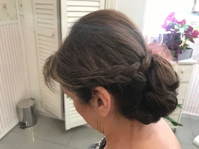 Mujer con cabello castaño oscuro recogido en un moño bajo trenzado, vista de perfil en una habitación luminosa.
