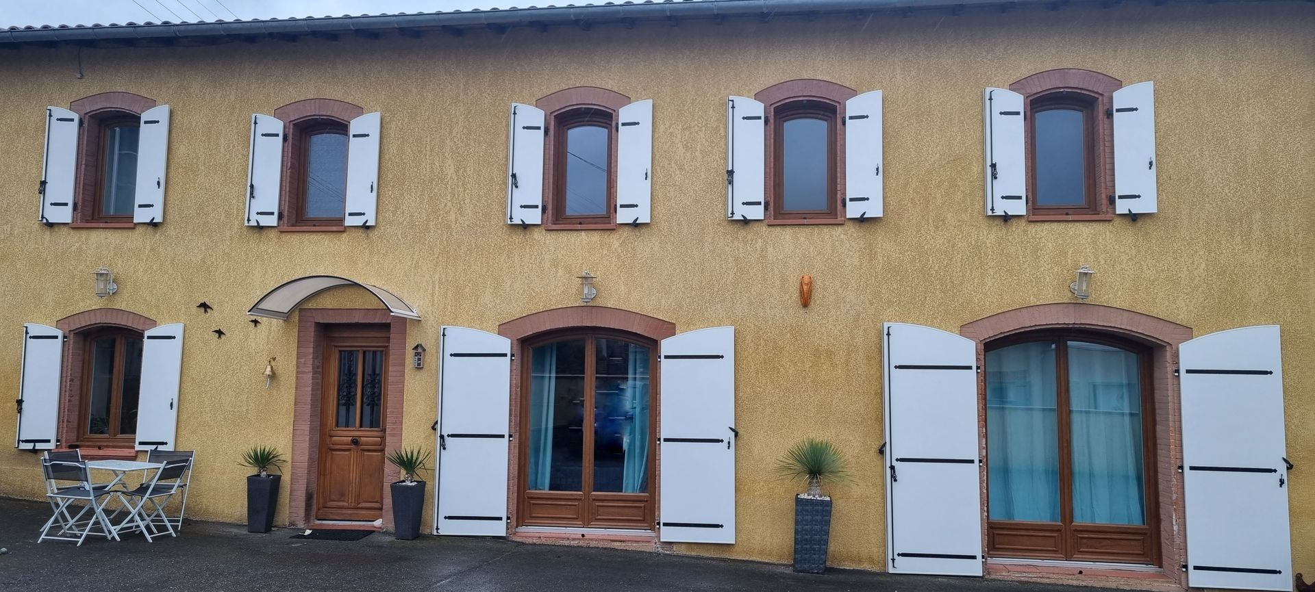 Fenêtre avec un volet roulant blanc solaire, fixée sur un mur couleur pêche et avec des volets battants bois.