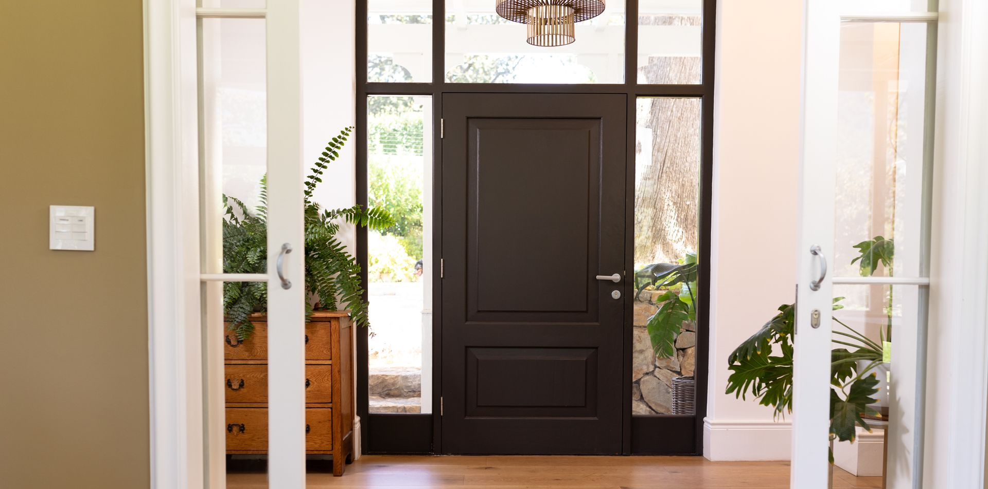 Entrée avec porte brun foncé, impostes vitrées et parquet clair. Des portes doubles blanches ouvertes encadrent la vue.