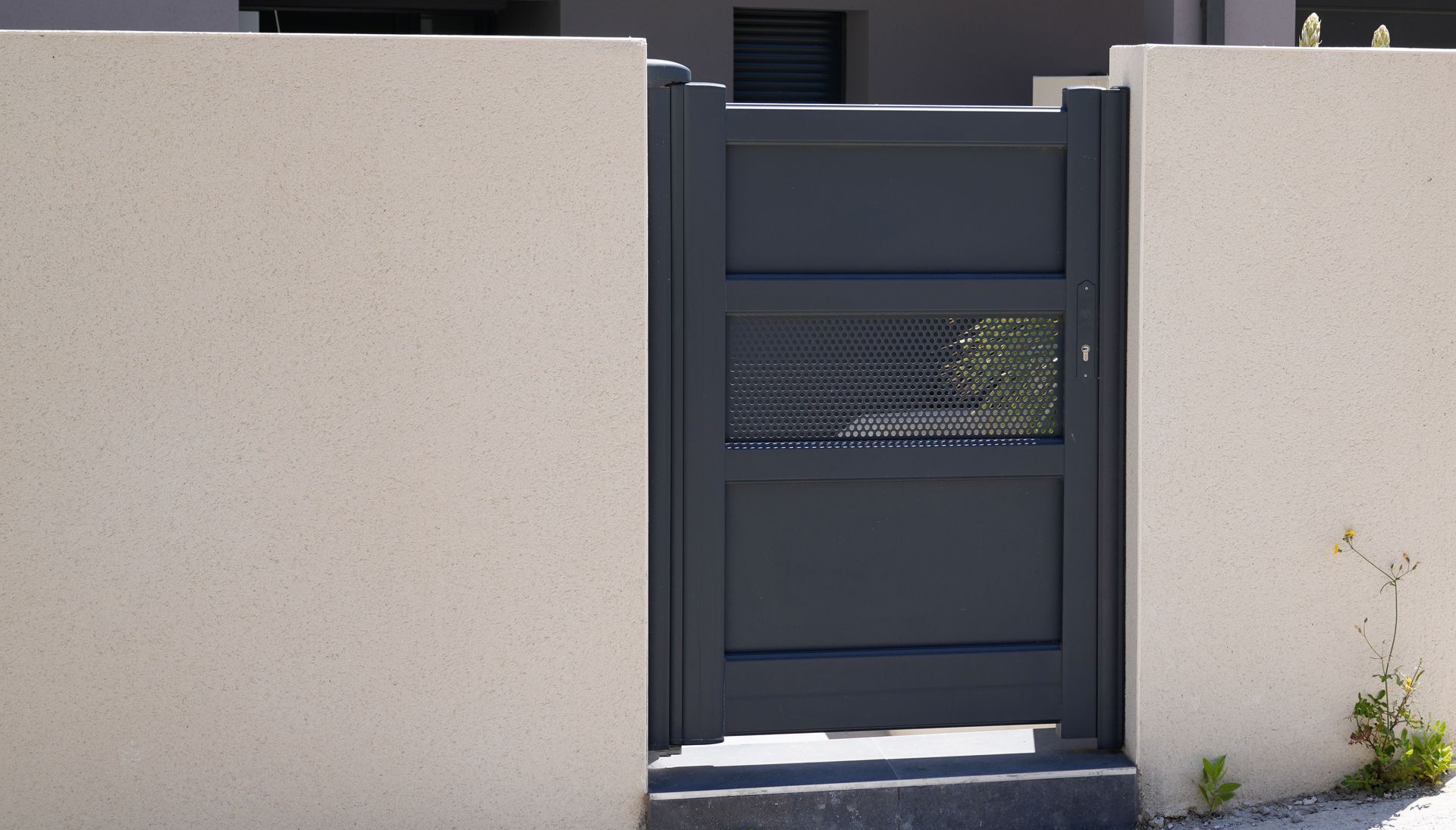 Portail en métal gris foncé installé entre deux murs beiges.