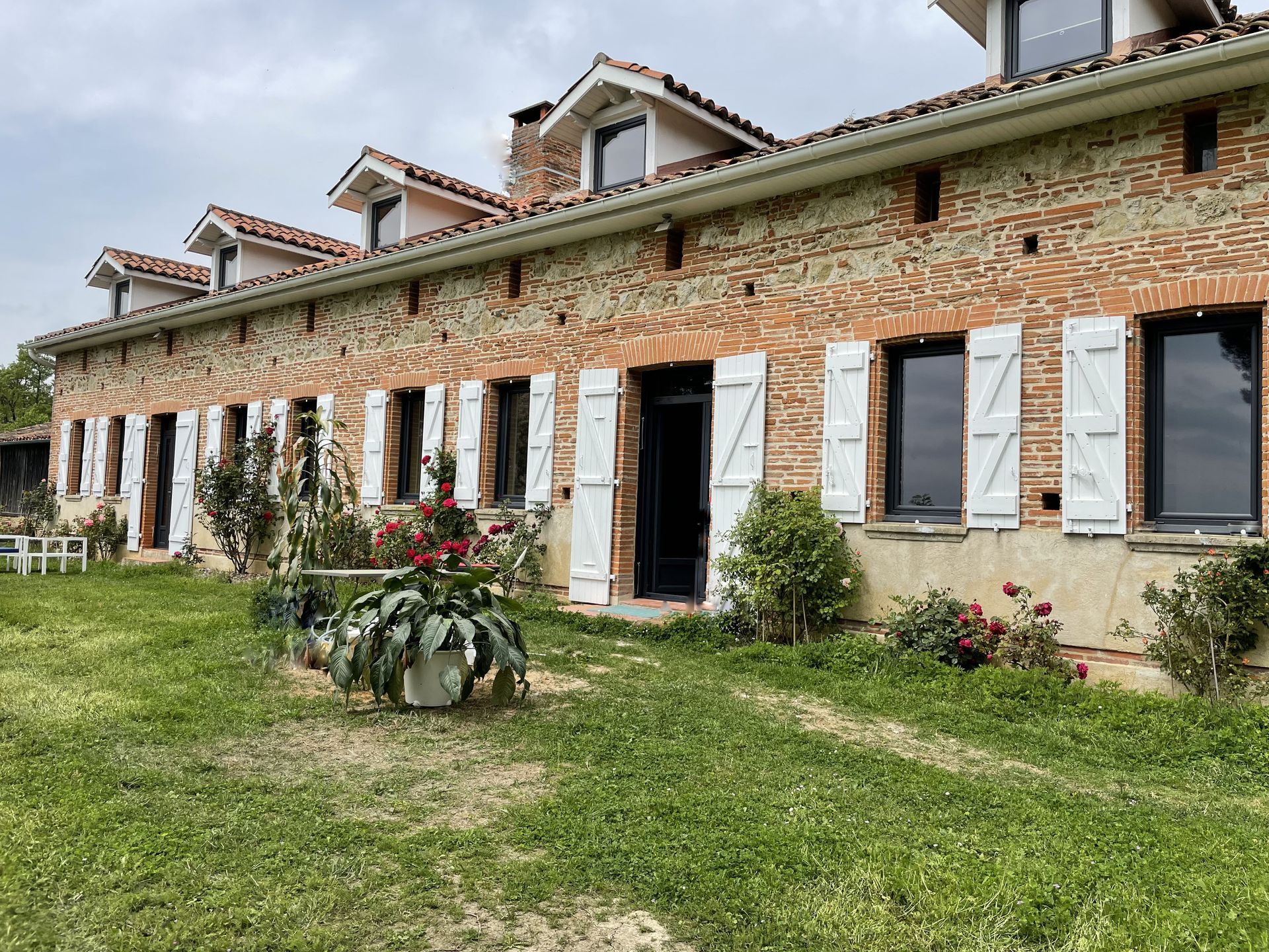 Maison en brique rouge avec des volets en bois blanc et fenêtre grise