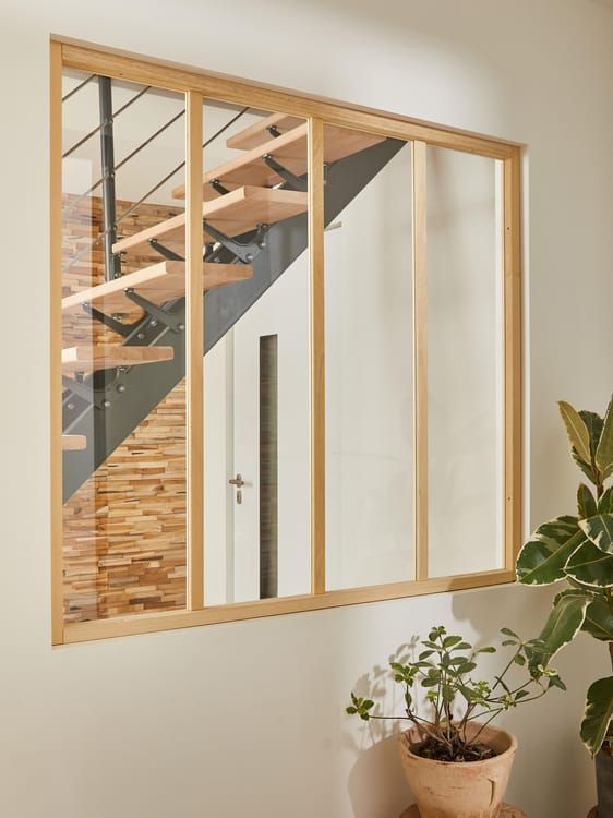 Fenêtre à cadre en bois et panneaux de verre donnant sur un escalier, une porte et un mur de briques.