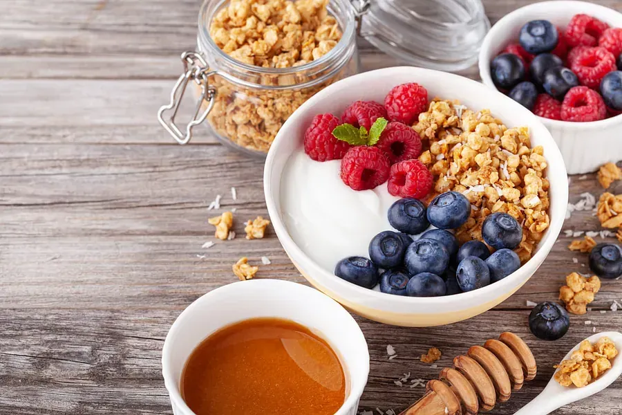 Un tazón de granola, yogur, arándanos, frambuesas y miel sobre una mesa de madera.