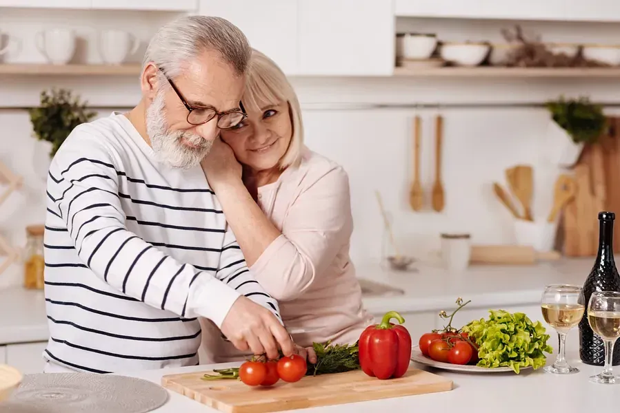 Un hombre y una mujer están cortando verduras en una tabla de cortar en una cocina.