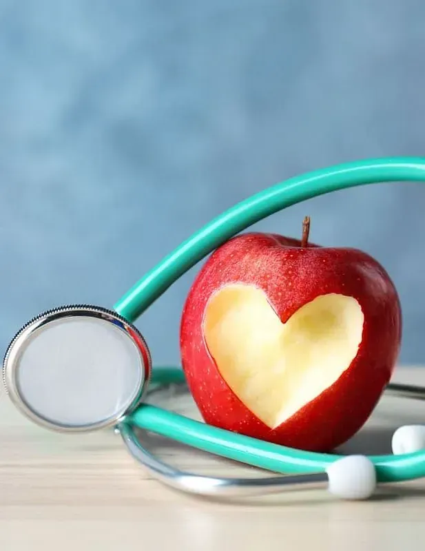 Una manzana con un corazón cortado junto a un estetoscopio
