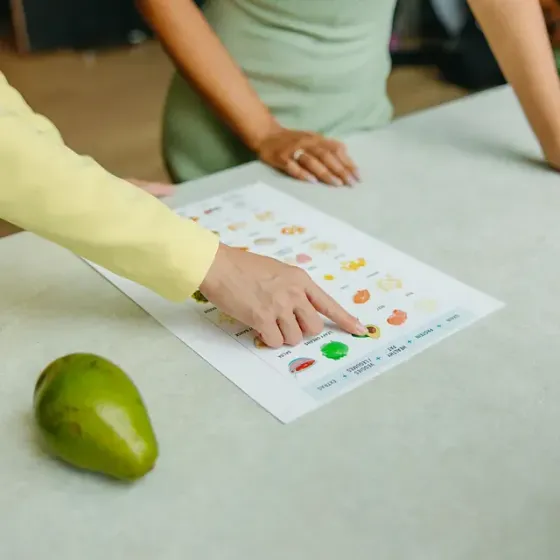 Una persona señala un trozo de papel que contiene frutas y verduras.