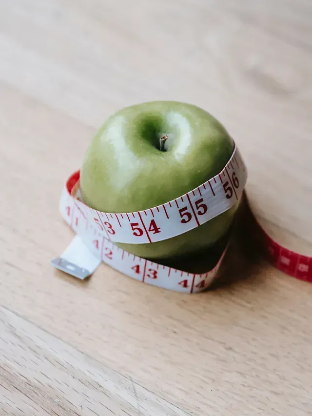 Una manzana verde está envuelta en una cinta métrica sobre una mesa de madera.