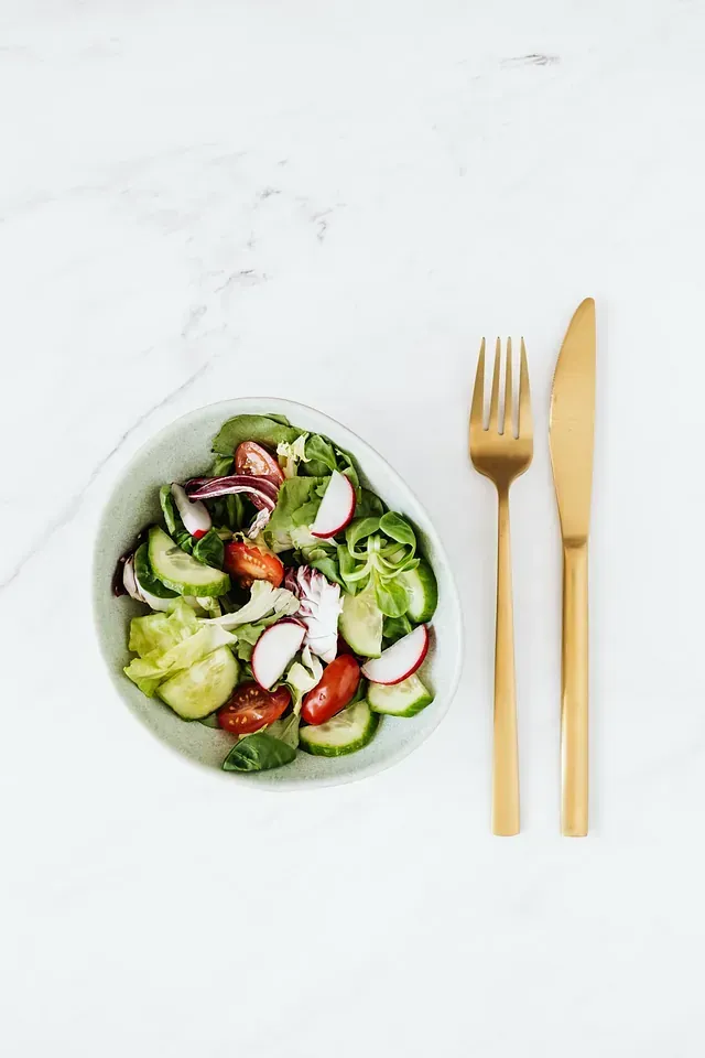 Un plato de lleno de verduras junto a un tenedor y un cuchillo.