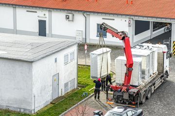 Una grúa está levantando un contenedor de un camión frente a un edificio.