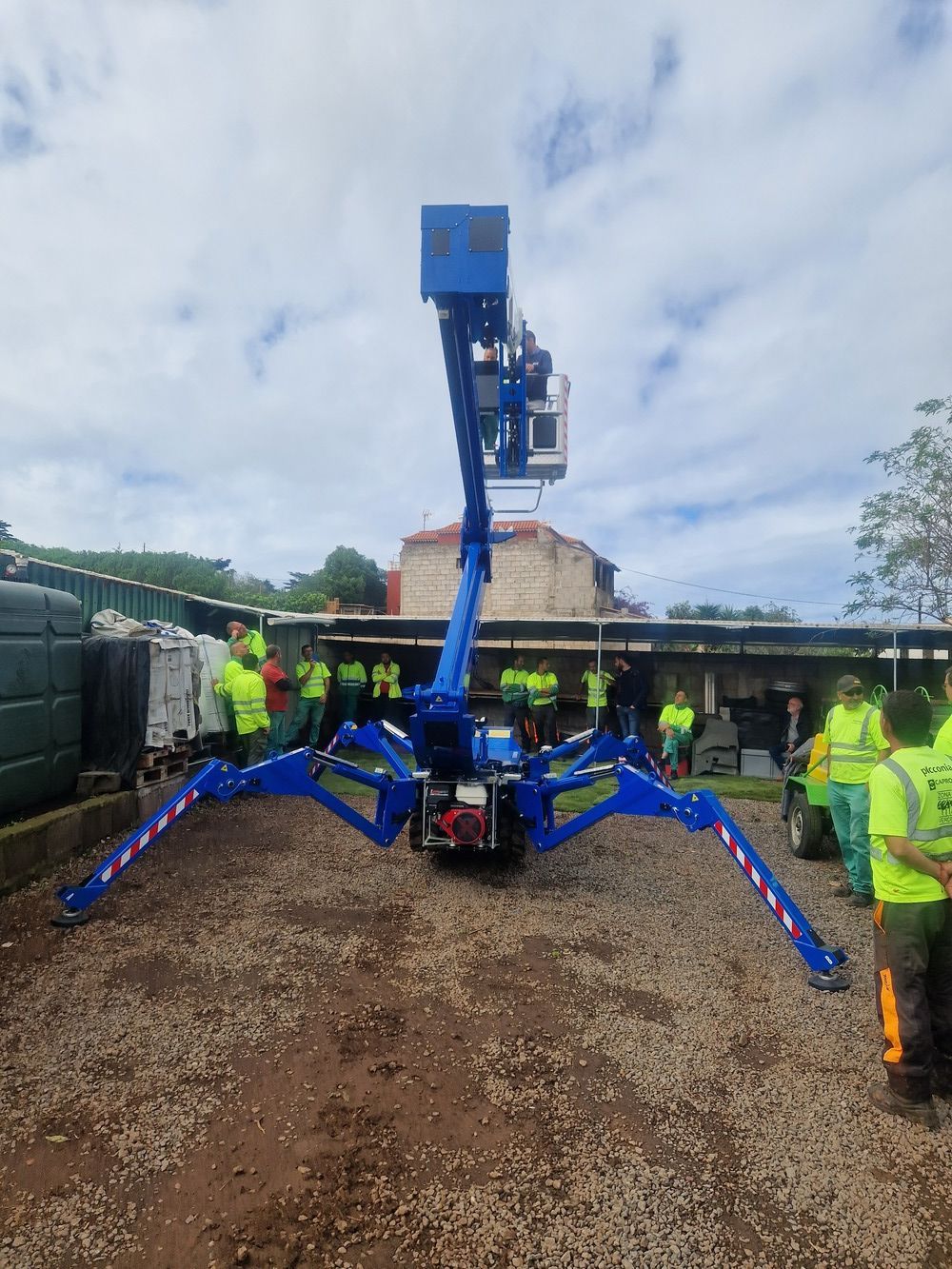 Un grupo de personas se encuentra de pie alrededor de un elevador araña azul.