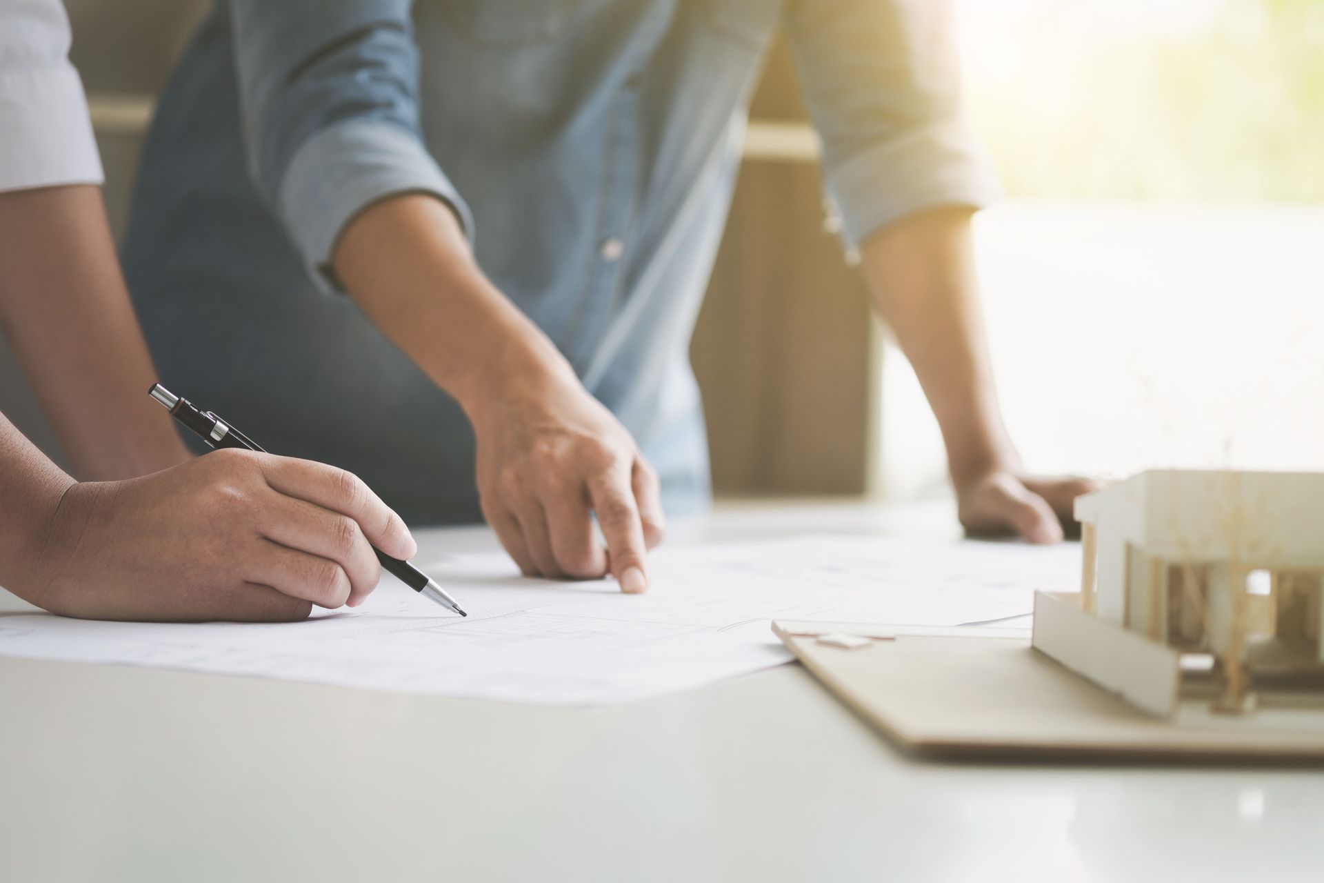 Deux personnes dessinent des plans sur papier à une table à côté d'une petite maquette de bâtiment.