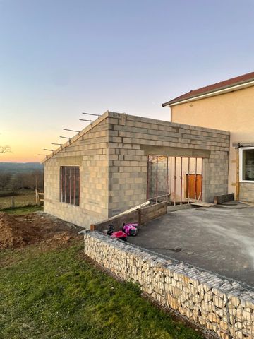 Extension en pierre en cours de construction, attenante à une maison au coucher du soleil, avec une terrasse en béton et un jardin enherbé