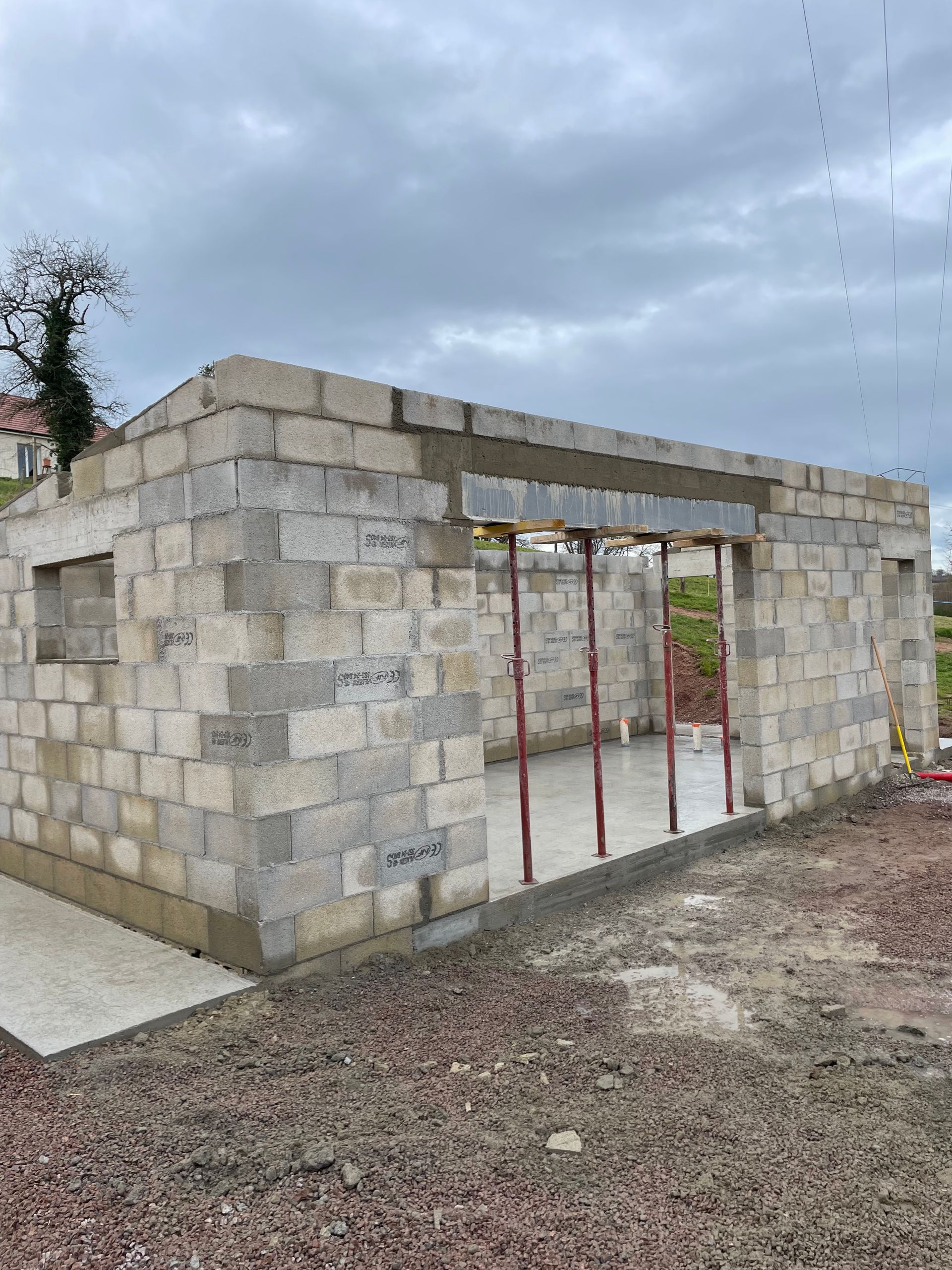 Structure en parpaings partiellement construite, avec une porte ouverte et un ciel nuageux