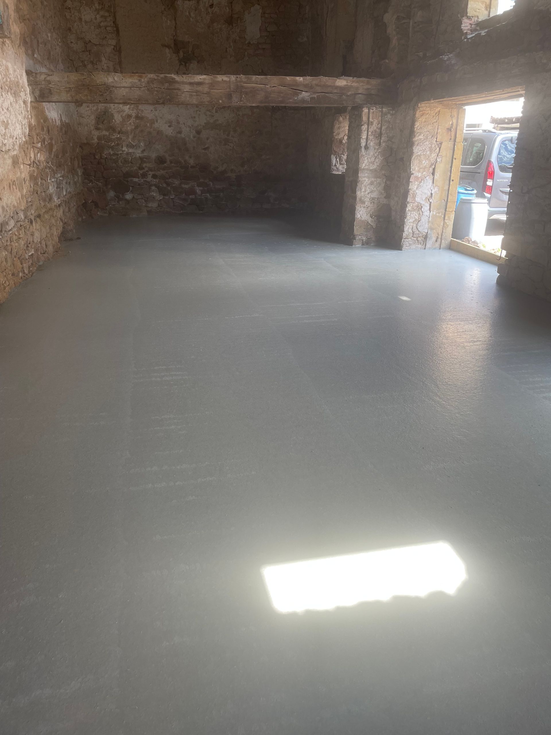Pièce vide aux murs et au sol en béton brut, éclairée par un rayon de soleil près de l'entrée.