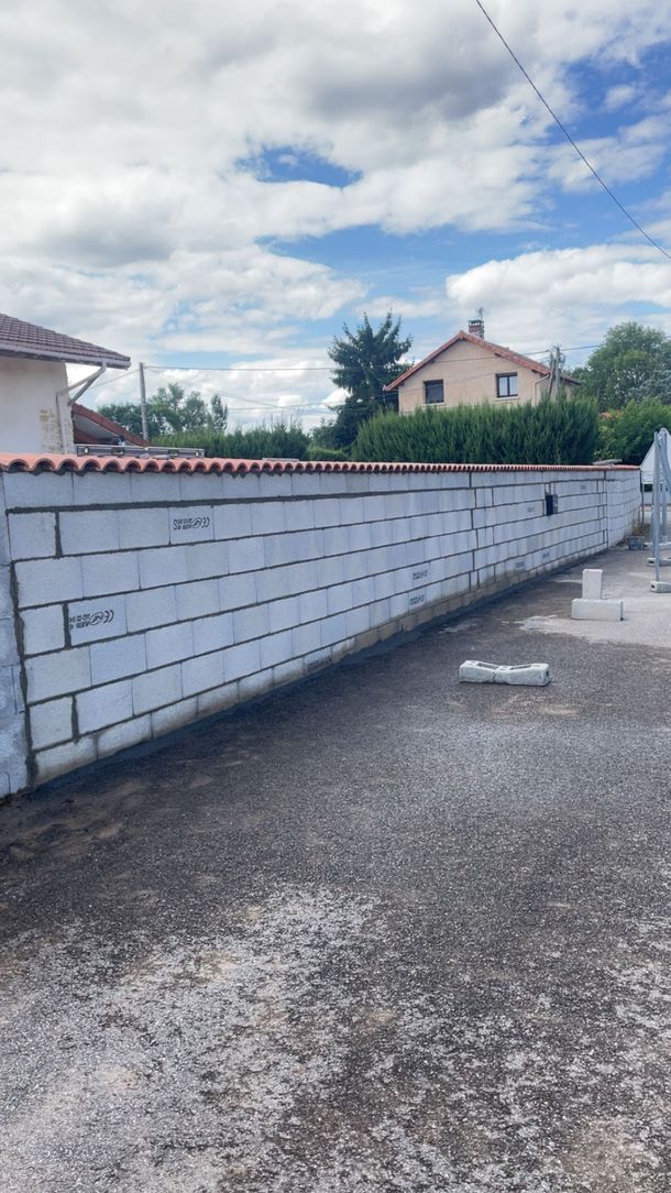 Long mur de maçonnerie blanche bordant une allée de gravier sous un ciel partiellement nuageux dans une cour résidentielle.
