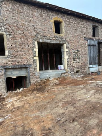 Ancien bâtiment en pierre en construction, avec des portes ouvertes et un premier plan en terre battue.