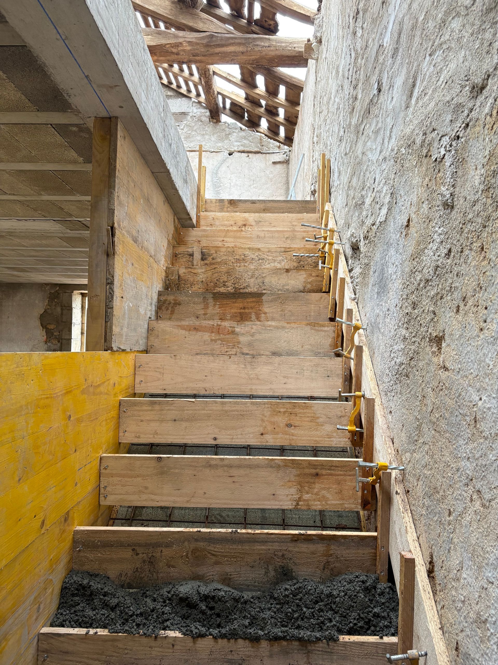 Escalier étroit en béton aux marches usées, mur jaune et murs à la texture rugueuse, baigné de lumière naturelle.