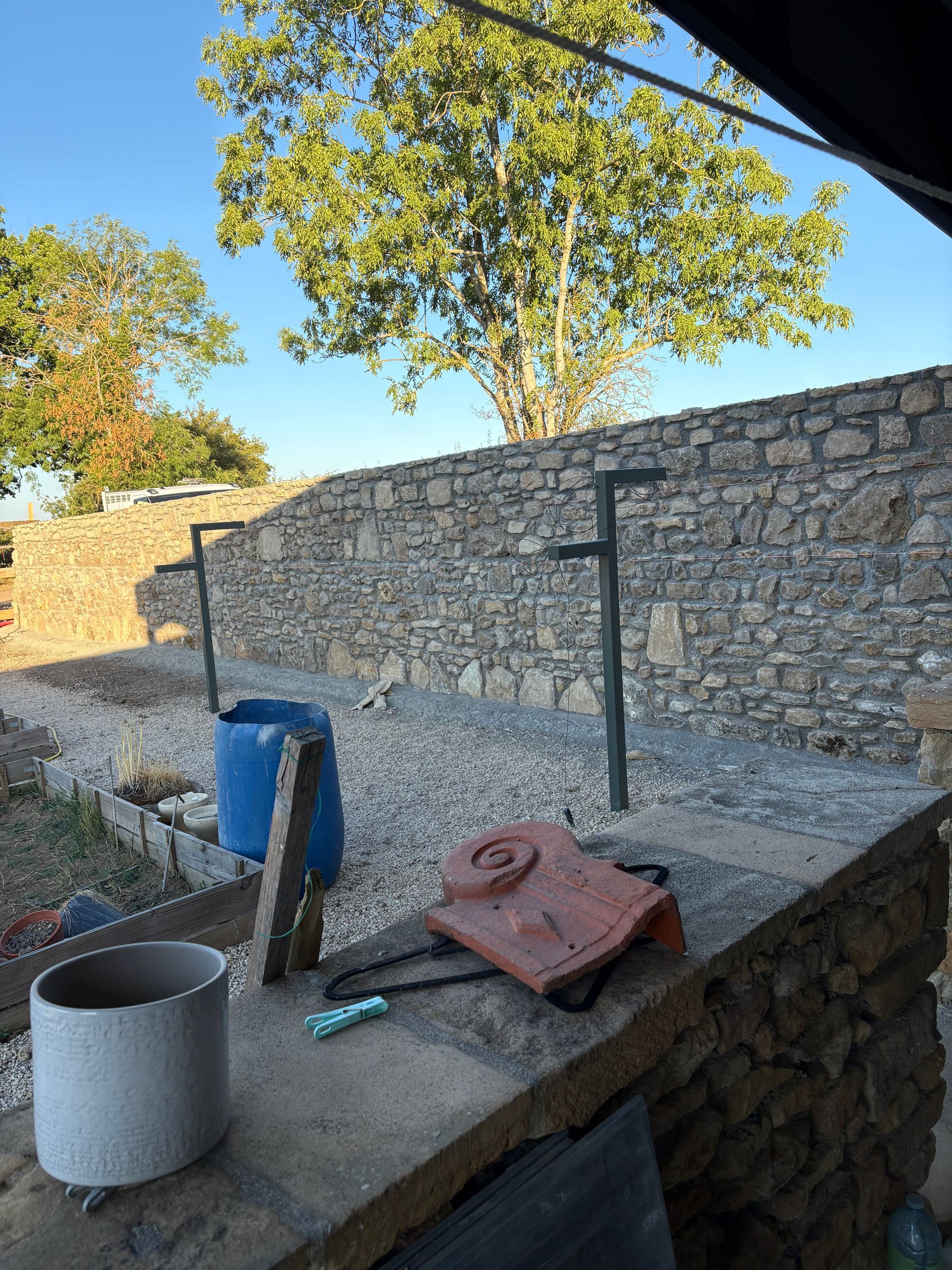 Terrasse en pierre avec un seau bleu, un pot en métal et des outils de jardinage sous un ciel ensoleillé