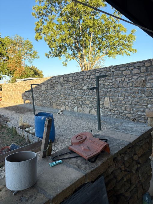 Terrasse en pierre avec un seau bleu, un pot en métal et des outils de jardinage sous un ciel ensoleillé