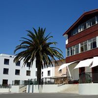 Palmera frente a dos edificios con fachadas blancas y rojas, contra un cielo azul claro.
