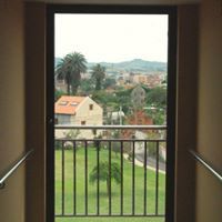 Vista desde una puerta: césped verde, edificios, árboles y colinas lejanas.