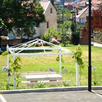 Pérgola blanca con una mesa de picnic en un parque con césped, un edificio visible al fondo.
